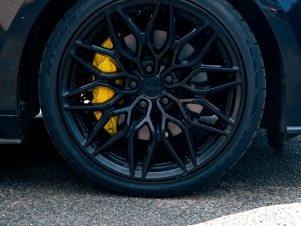 Yellow brake caliper and rotor visible through the spokes of a black wheel on a Ford Mustang GT