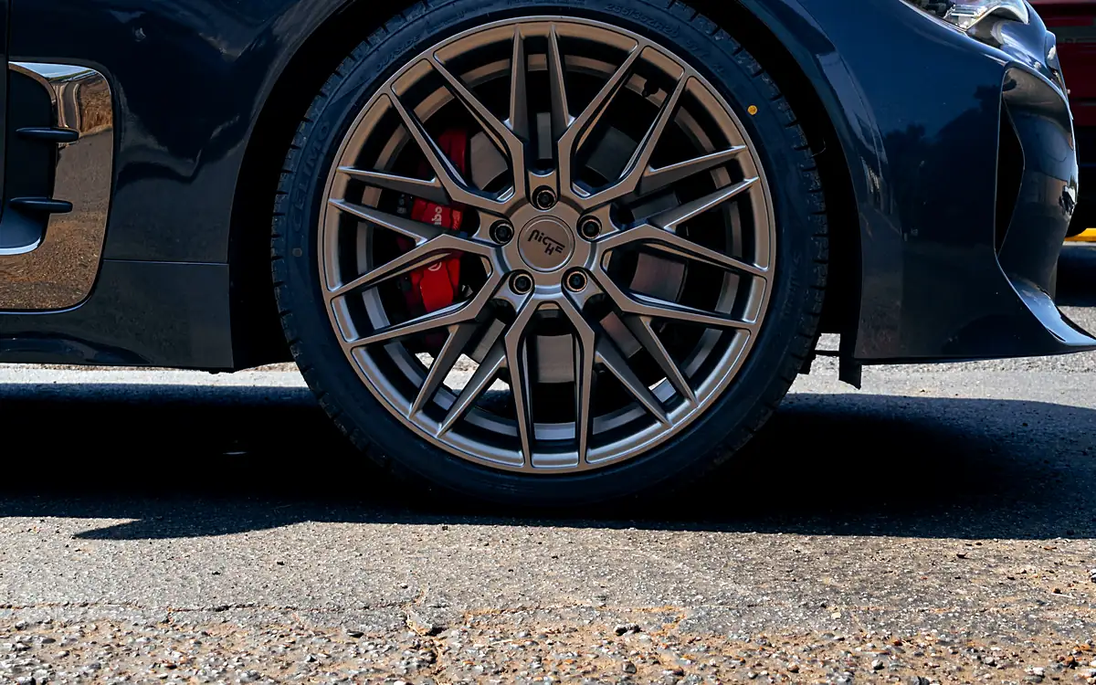 Red brake caliper behind a bronze wheel on a dark gray Kia Stinger