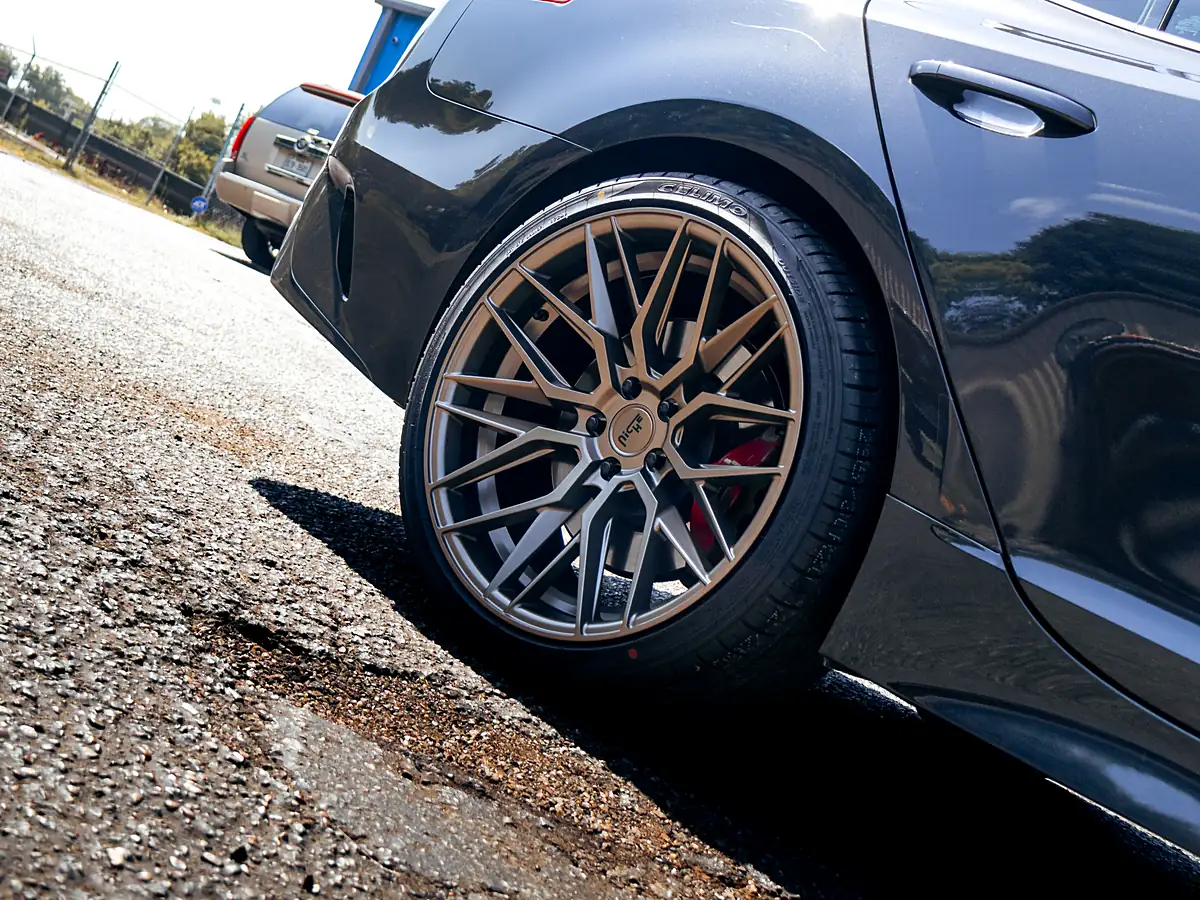 Low angle of a bronze wheel and tire on a dark gray Kia Stinger at the Wheels Up Front shop