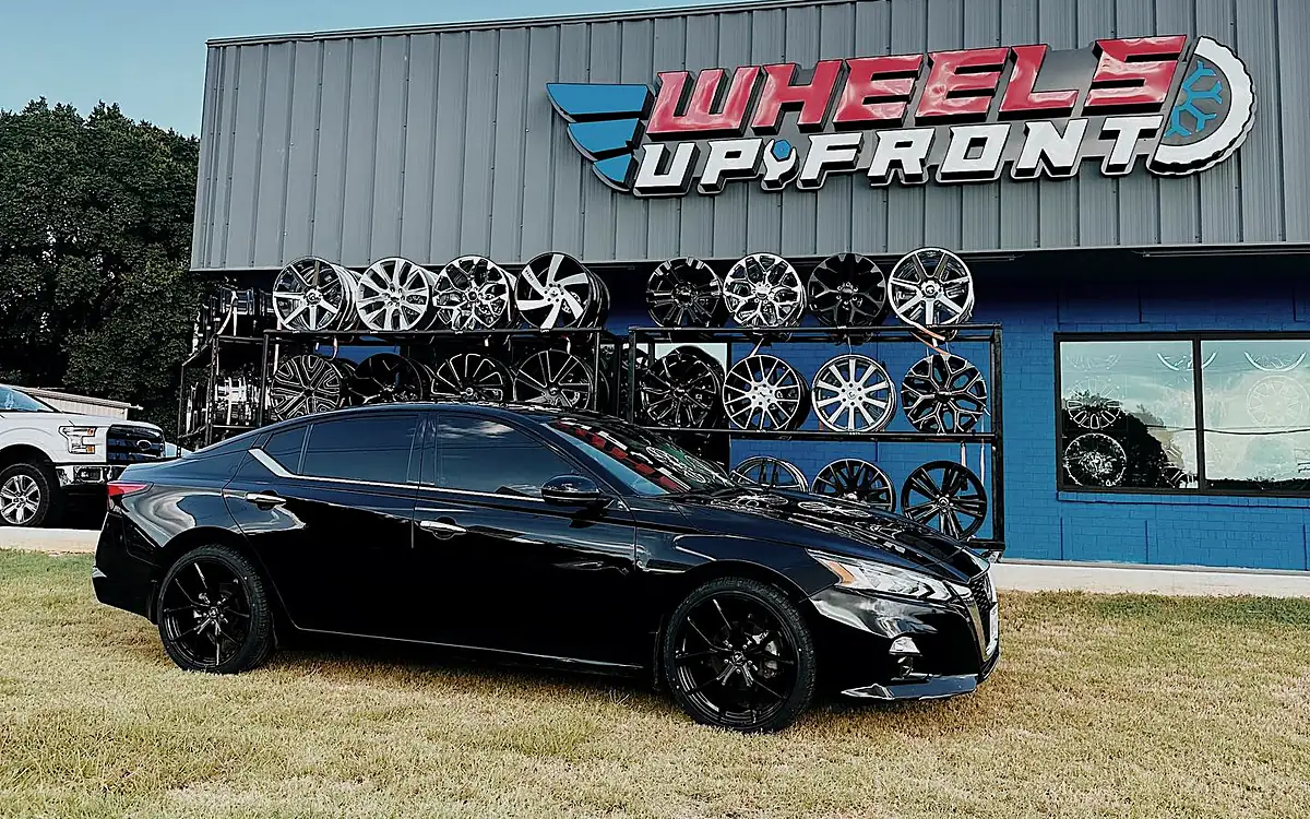 Black Nissan Altima on black wheels parked in front of the Wheels Up Front wheel wall