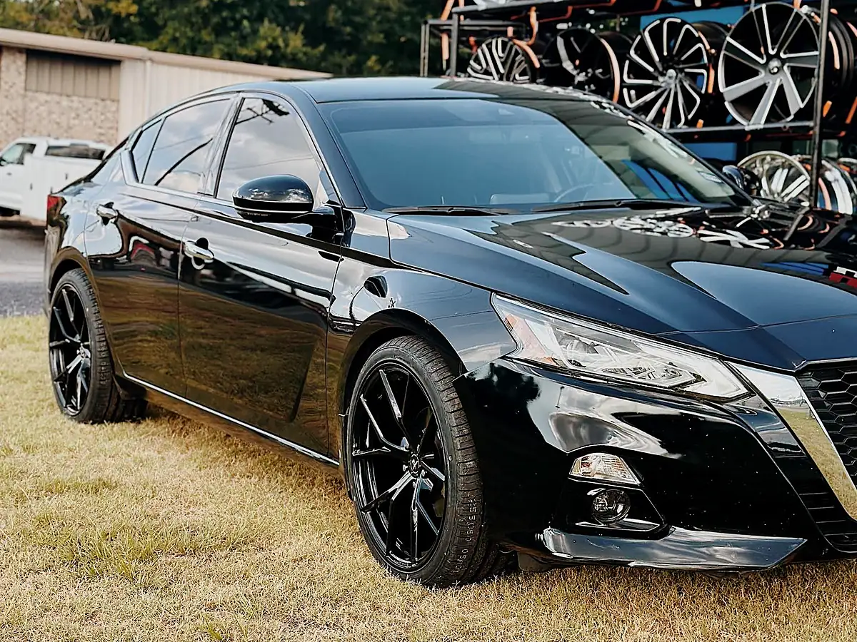 Front three-quarter view of a black Nissan Altima on black wheels outside the Wheels Up Front shop