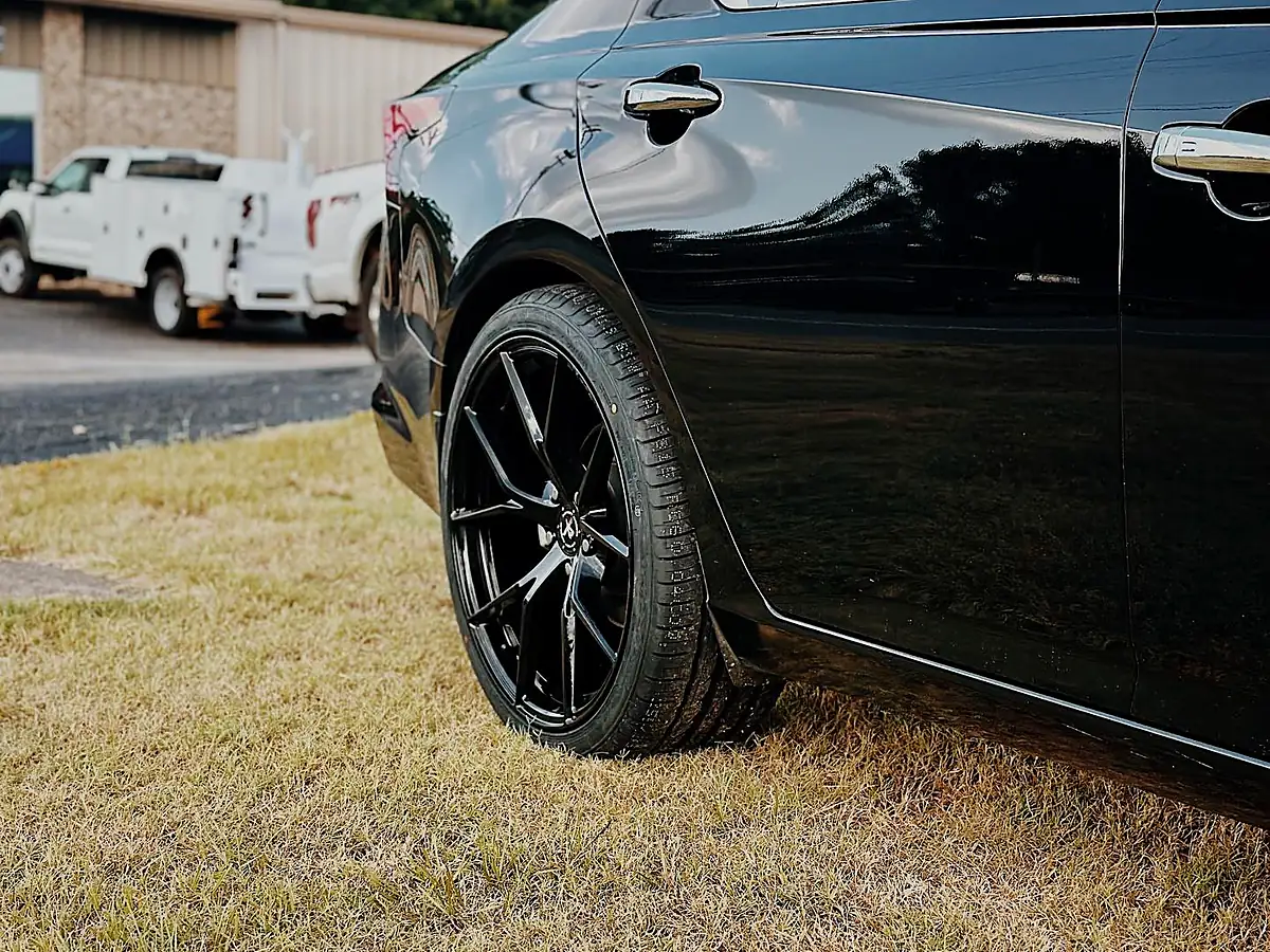 Rear black wheel and tire on a black Nissan Altima parked on grass