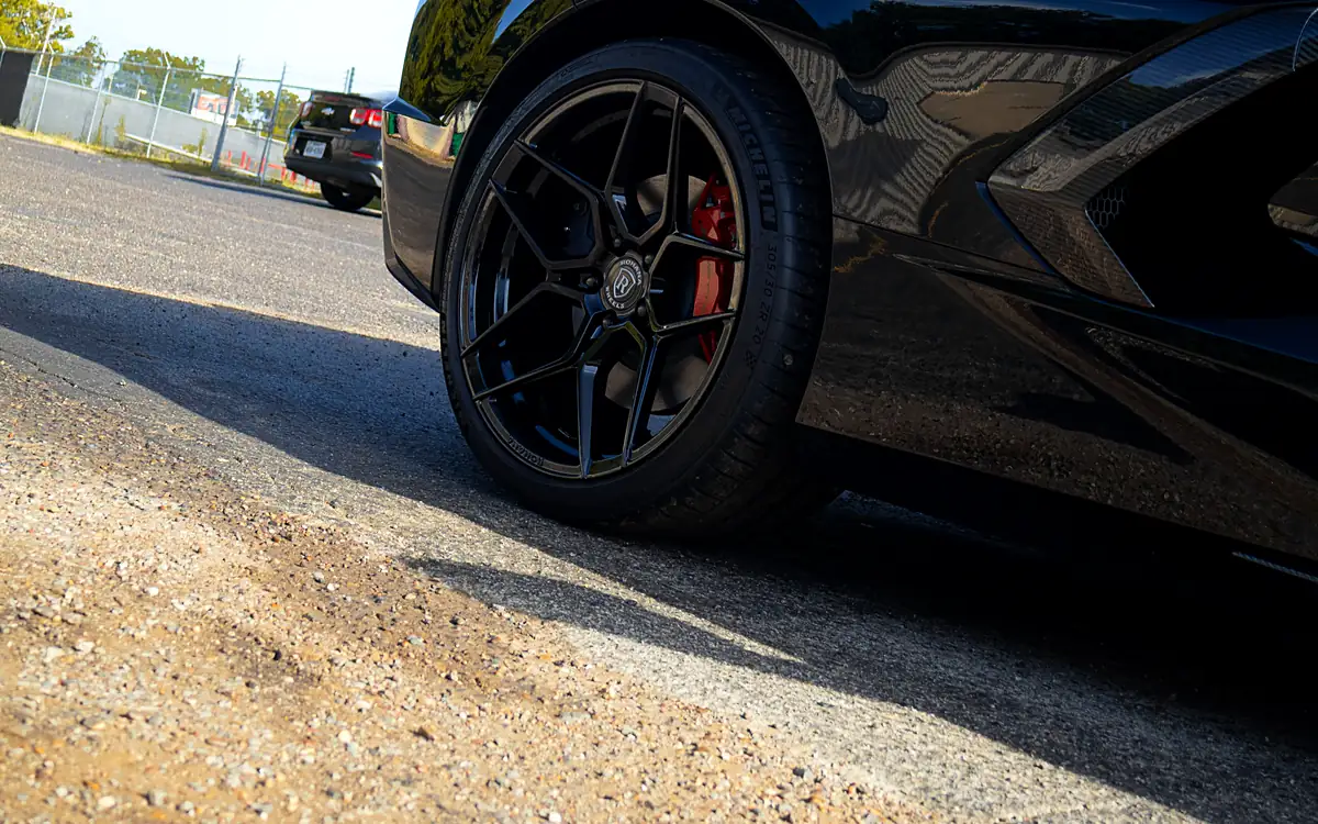 Red brake caliper behind a black wheel on a black Corvette C8, shot low at the Wheels Up Front shop