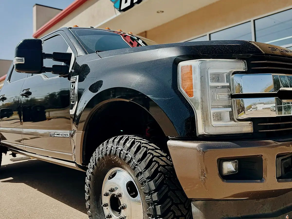 Mud-terrain tire on a polished wheel on the front of a black Ford F-350 dually outside the Wheels Up Front Tyler shop
