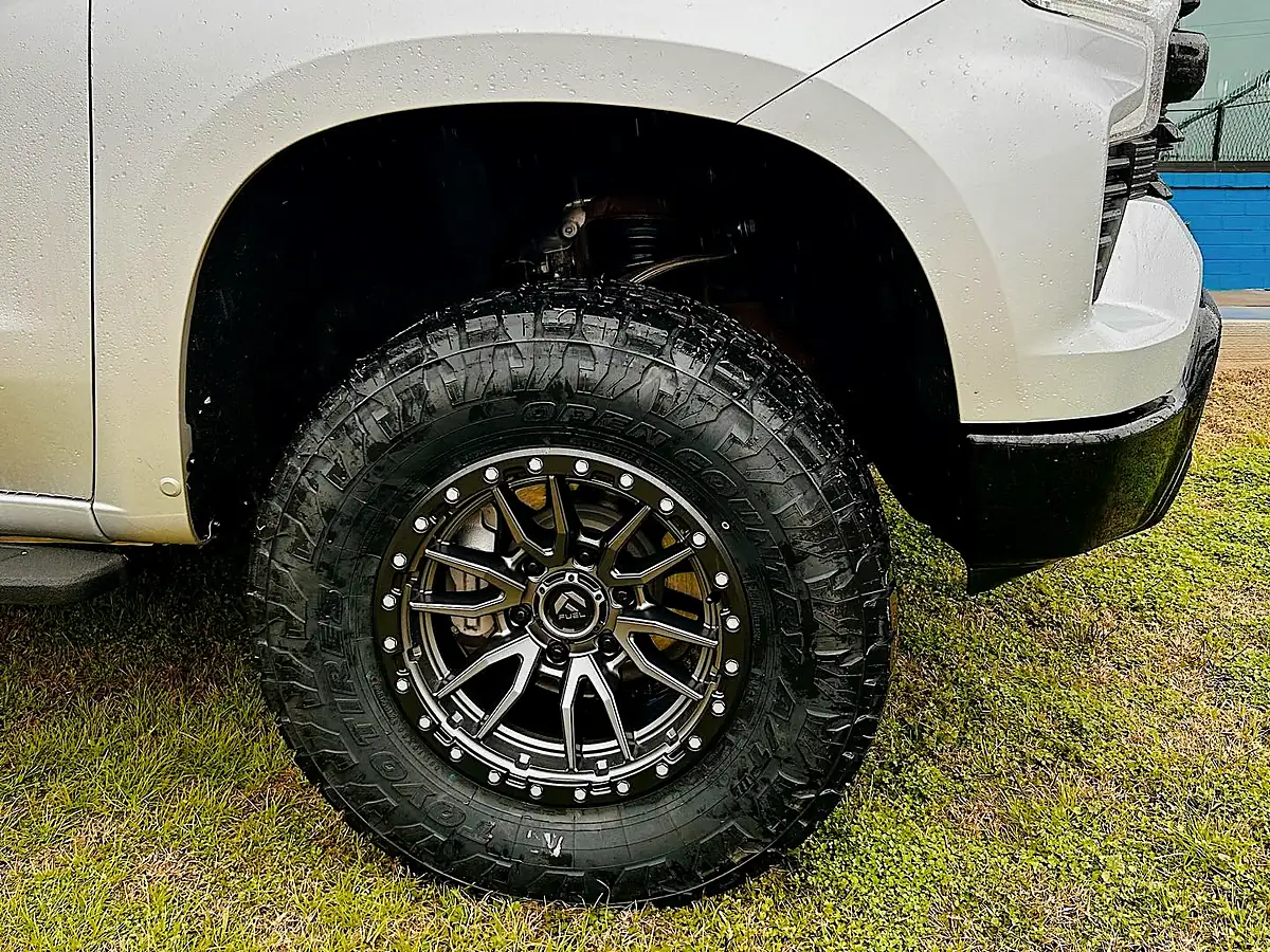 Fresh all-terrain tire tread on a black Fuel wheel on a white Chevy Silverado parked on grass