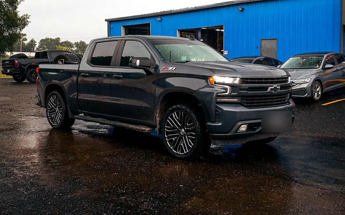Leveled gray Chevy Silverado 1500 Z71 on 24 inch black and milled wheels in the Wheels Up Front lot after rain