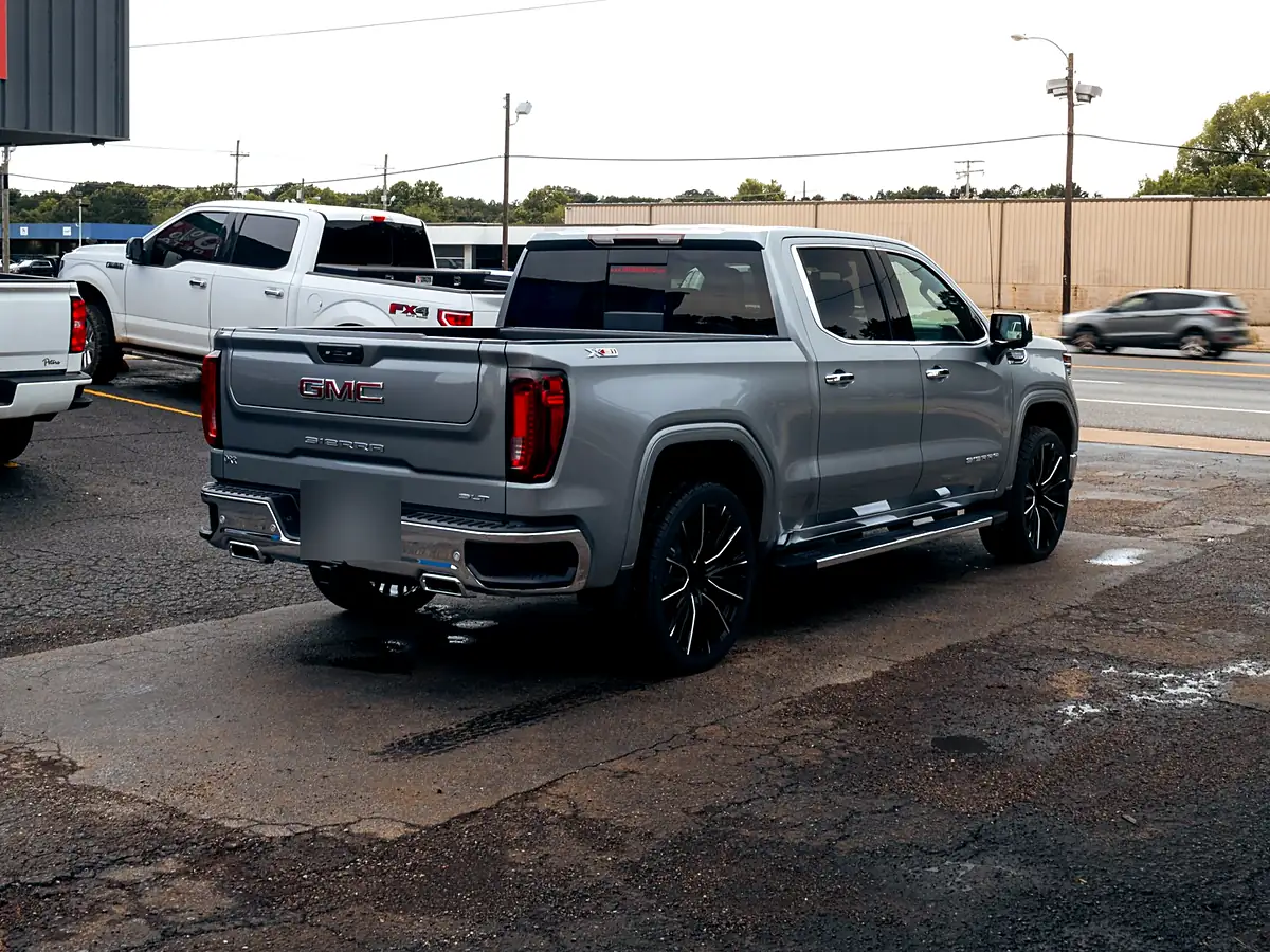 Rear three-quarter view of a silver 2026 GMC Sierra 1500 with a level kit and black 24 inch wheels in the Wheels Up Front lot