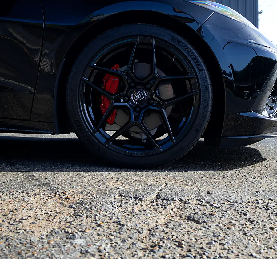 Red brake caliper behind a gloss black wheel on a black Corvette C8 outside the Wheels Up Front shop