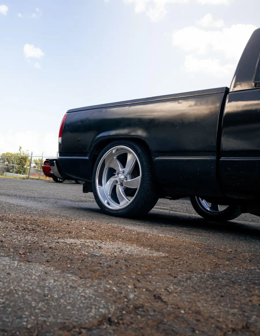 Slammed black Chevy OBS pickup on polished 22 inch US Mags wheels, shot low from the rear wheel